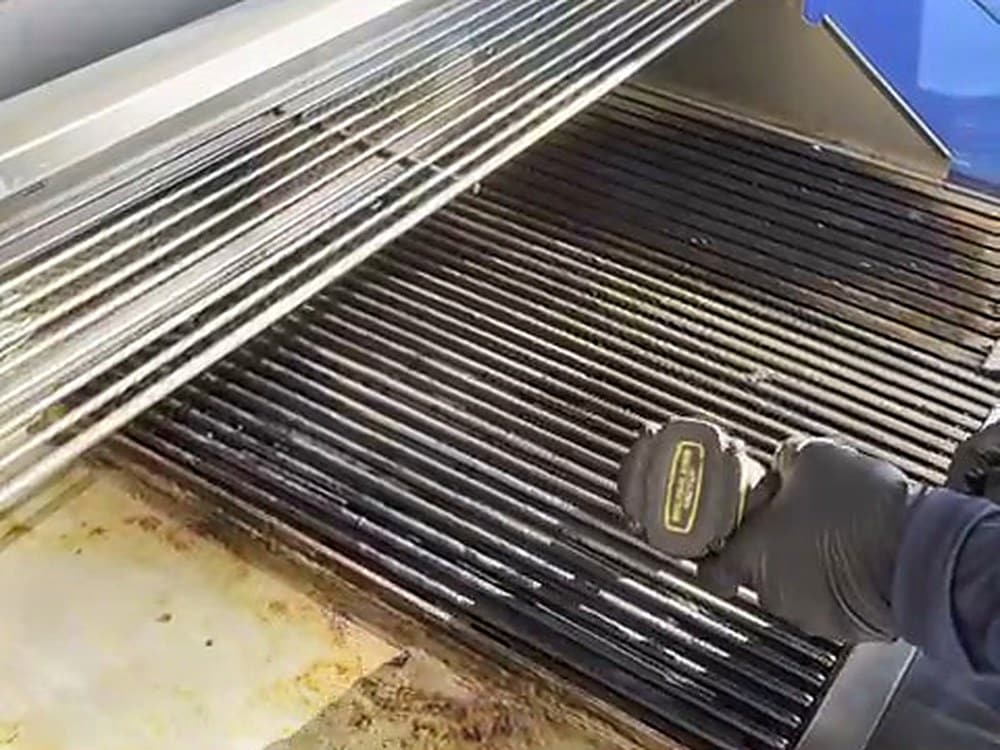 Technician using a drill brush on BBQ grill grates during a Brisbane BBQ clean