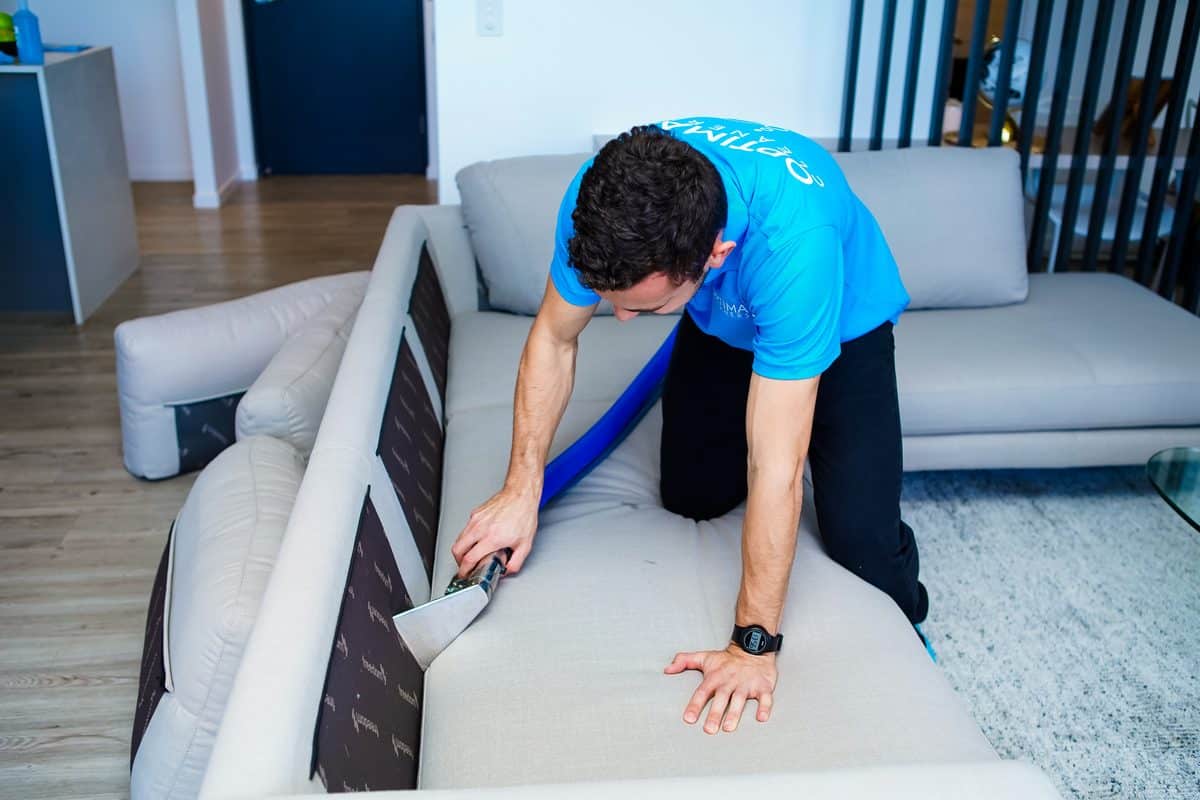 Optima Cleaners technician steam cleaning a fabric sofa with a hot water extraction wand