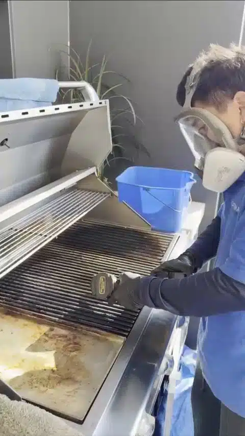 Optima Cleaners technician wearing a respirator while cleaning a BBQ